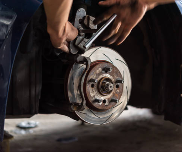 A mechanic is repairing a car's braking system, using a wrench to adjust the brake caliper on a ventilated and slotted disc brake.