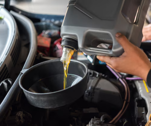 This image shows a hand pouring fresh motor oil from a plastic container into a drain pan during a vehicle oil change maintenance procedure.