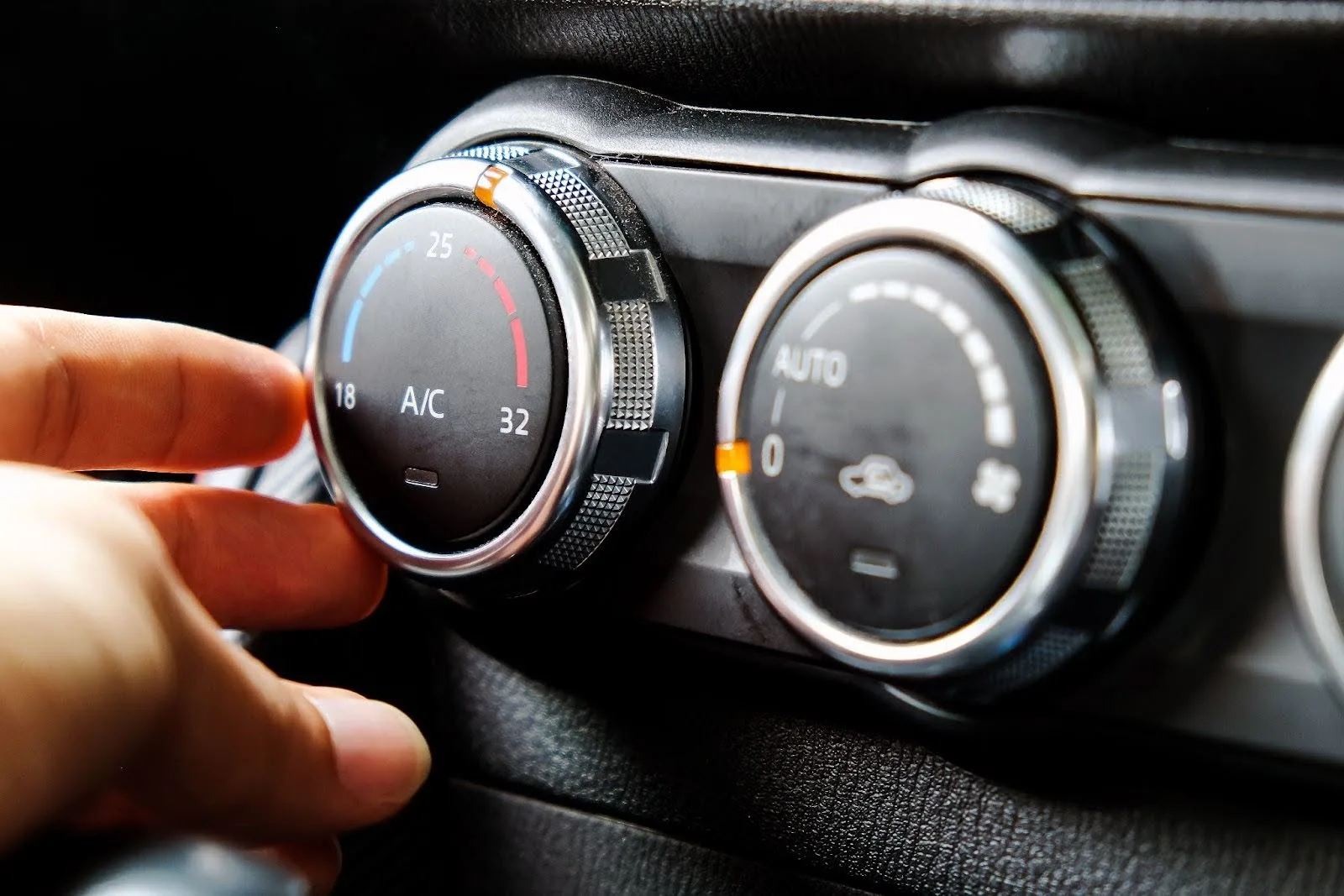 Hand adjusting car air conditioning dial with temperature range from 18 to 32 degrees on dashboard panel.