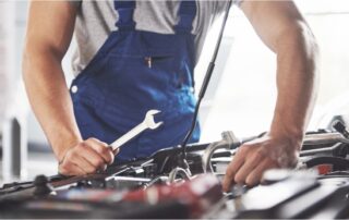 Auto mechanic in blue overalls repairing a car engine with a wrench inside a garage