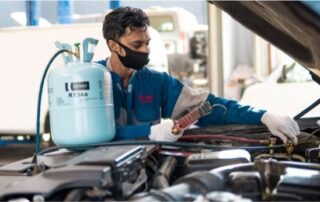 Mechanic performing air conditioning repair and gas refill on a car engine
