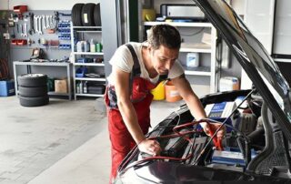Mechanic in blue overalls checking off items on a 'Vehicle Maintenance Checklist' clipboard in front of an open car engine.