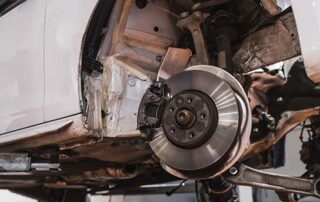 Exposed car suspension system and brake disc assembly on a vehicle lift during a maintenance check.