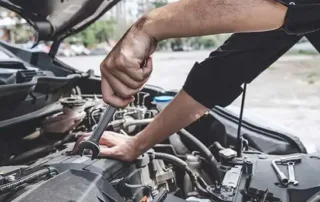 Mechanic using a wrench to perform maintenance on a car engine under the hood.