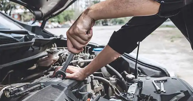 Mechanic using a wrench to perform maintenance on a car engine under the hood.